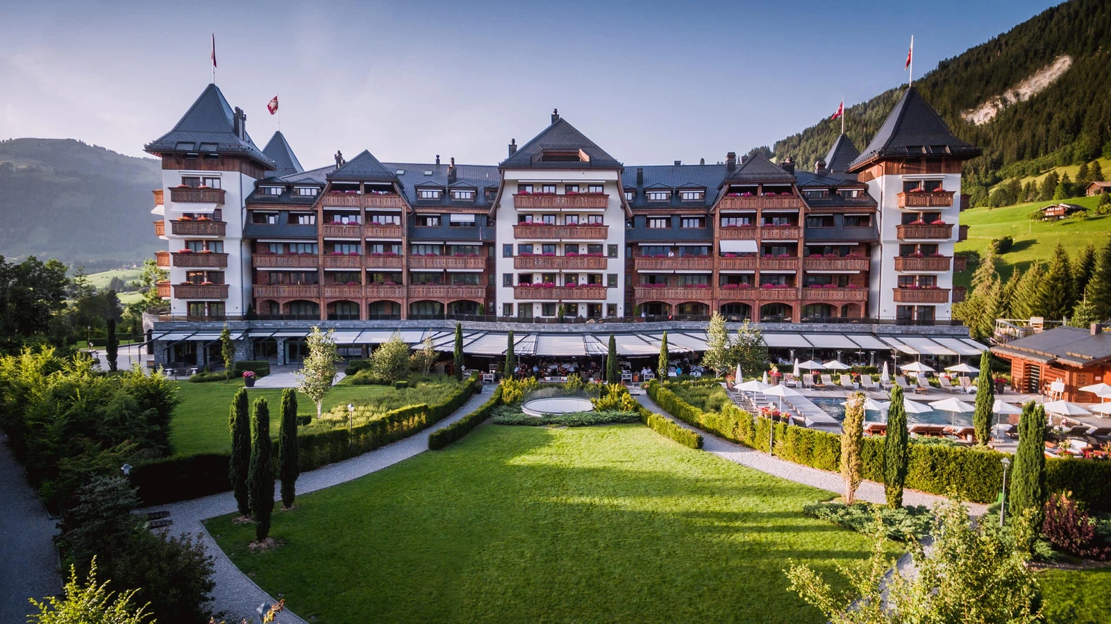 The complete facade of The Alpina Gstaad with its Alpine towers, gardens and pool