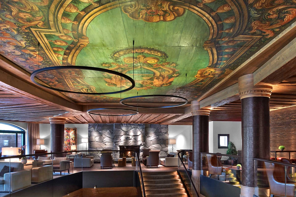 The Alpina Gstaad lounge with painted ceiling, stone fireplace and timber architecture