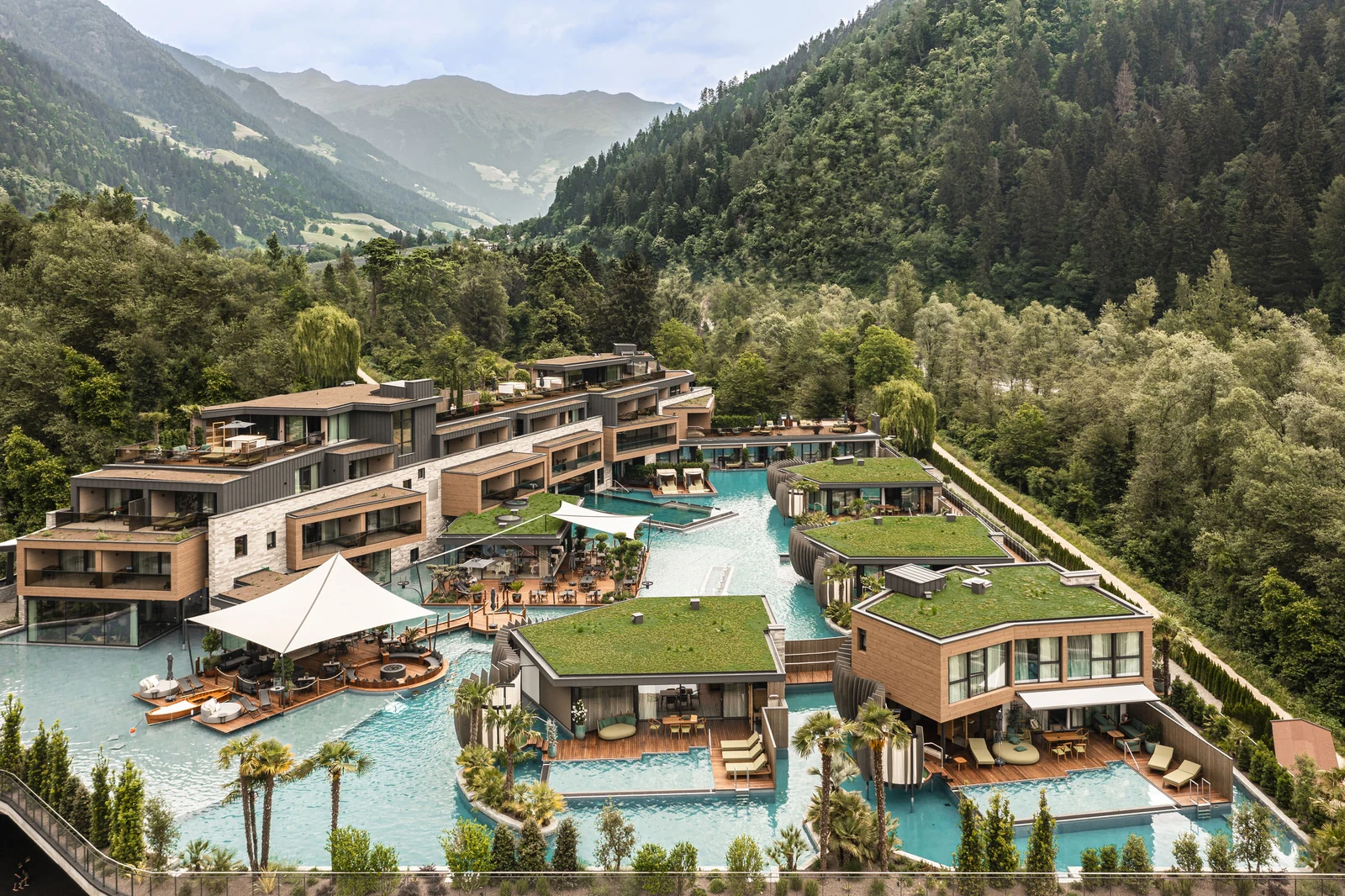 Elevated view of Quellenhof Luxury Resort Passeier with pools, villas and the Passeier Valley mountains